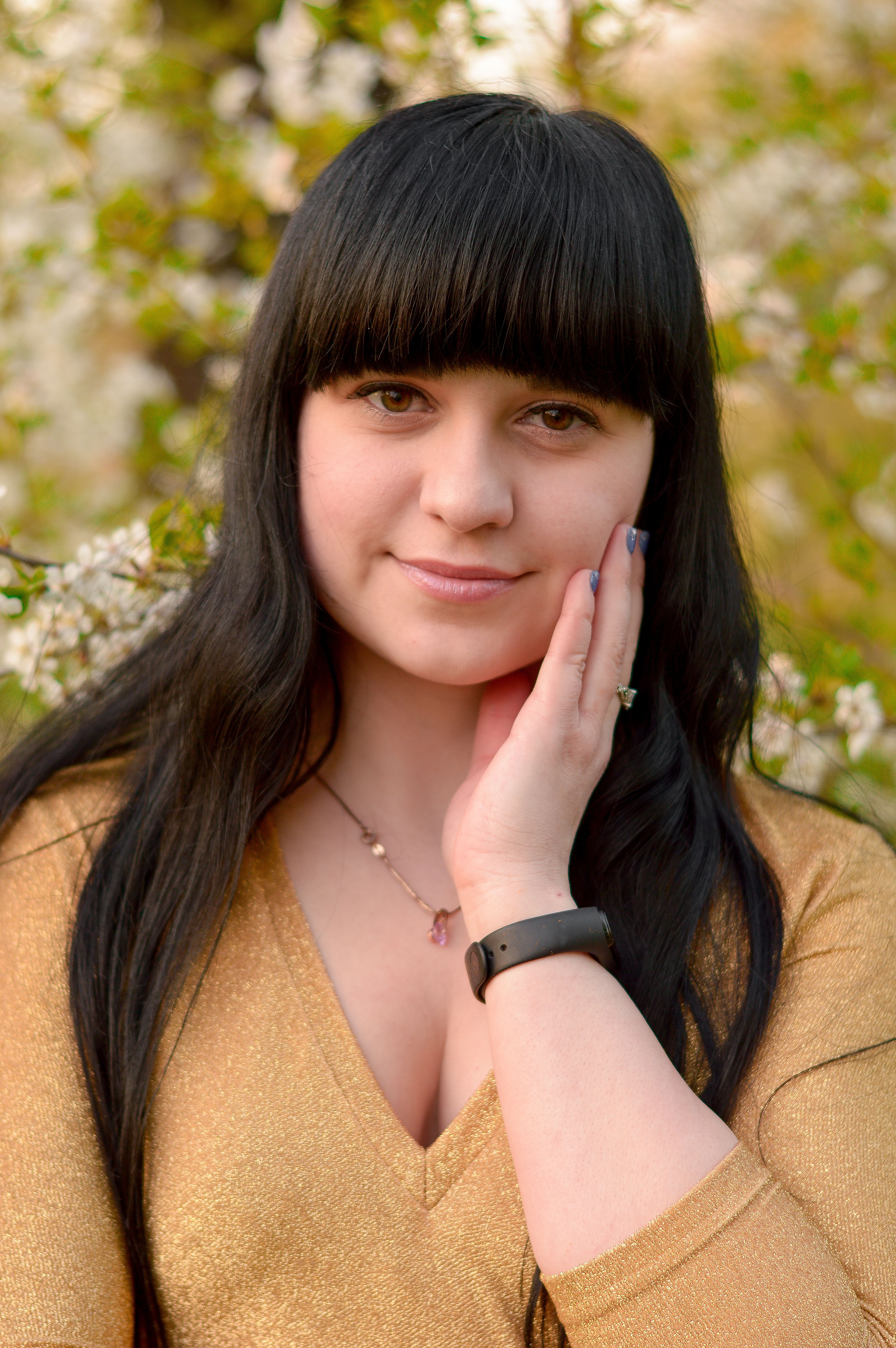 A serene portrait of a woman with long black hair in a spring garden, wearing a golden blouse.