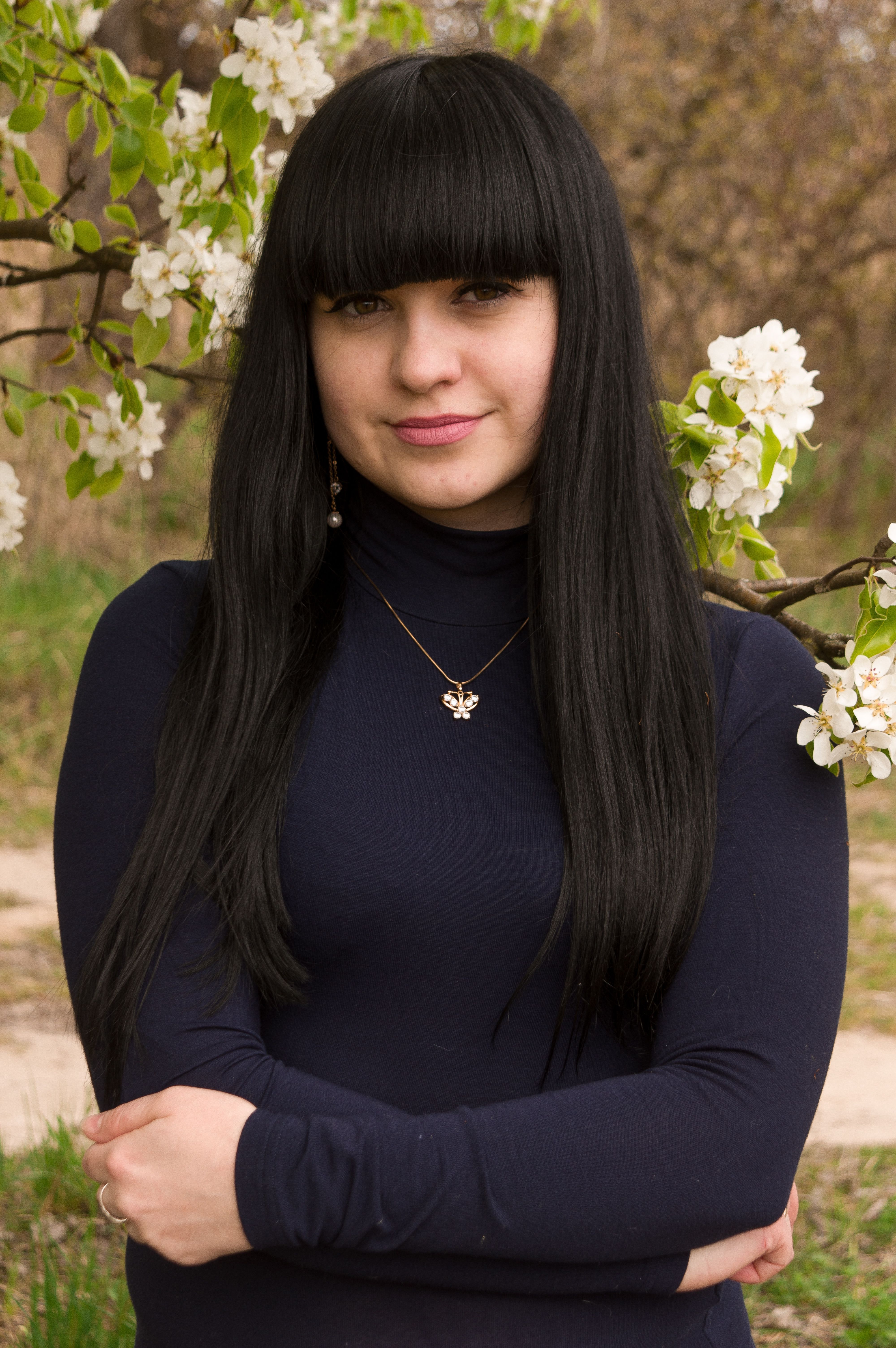 Portrait of a young woman with long black hair in a park during spring, surrounded by blooming flowers.