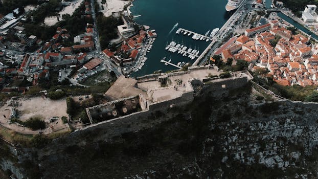 Stunning aerial view of Kotor's ancient castle and bustling marina with yachts.