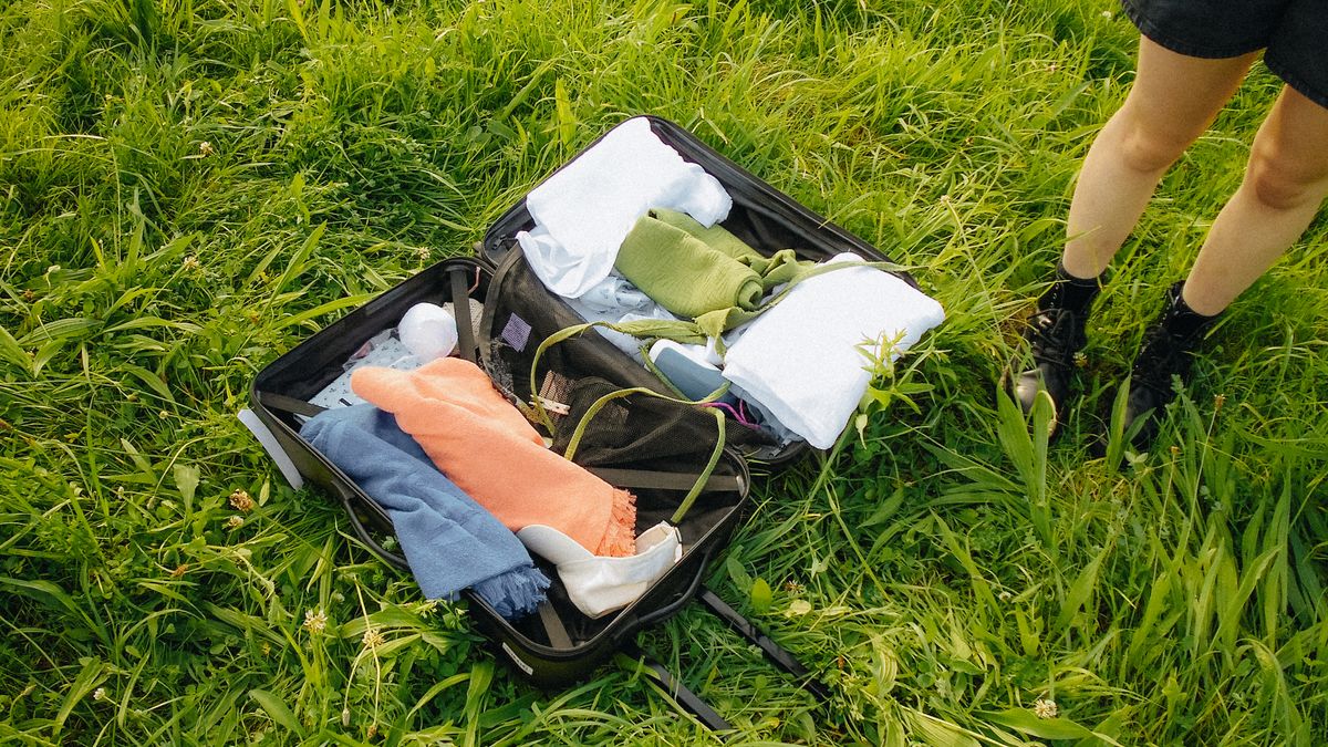 Open suitcase with travel essentials arranged outdoors on grass