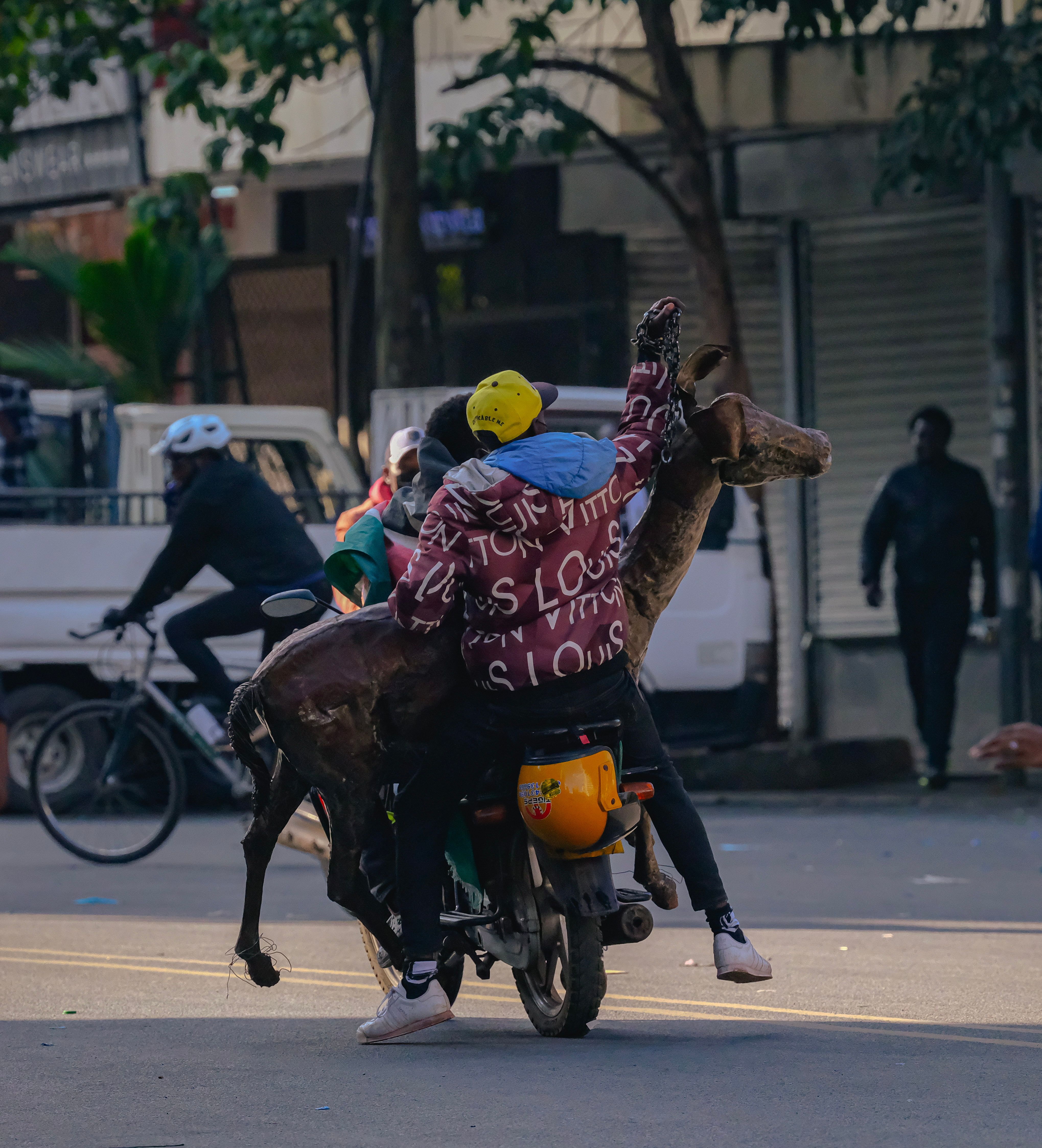 Motorcycle rider in Nairobi carrying a deer sculpture on a bustling street.