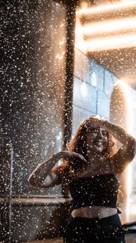 A young woman enjoys playful moments at night in a dazzling water spray under city lights.