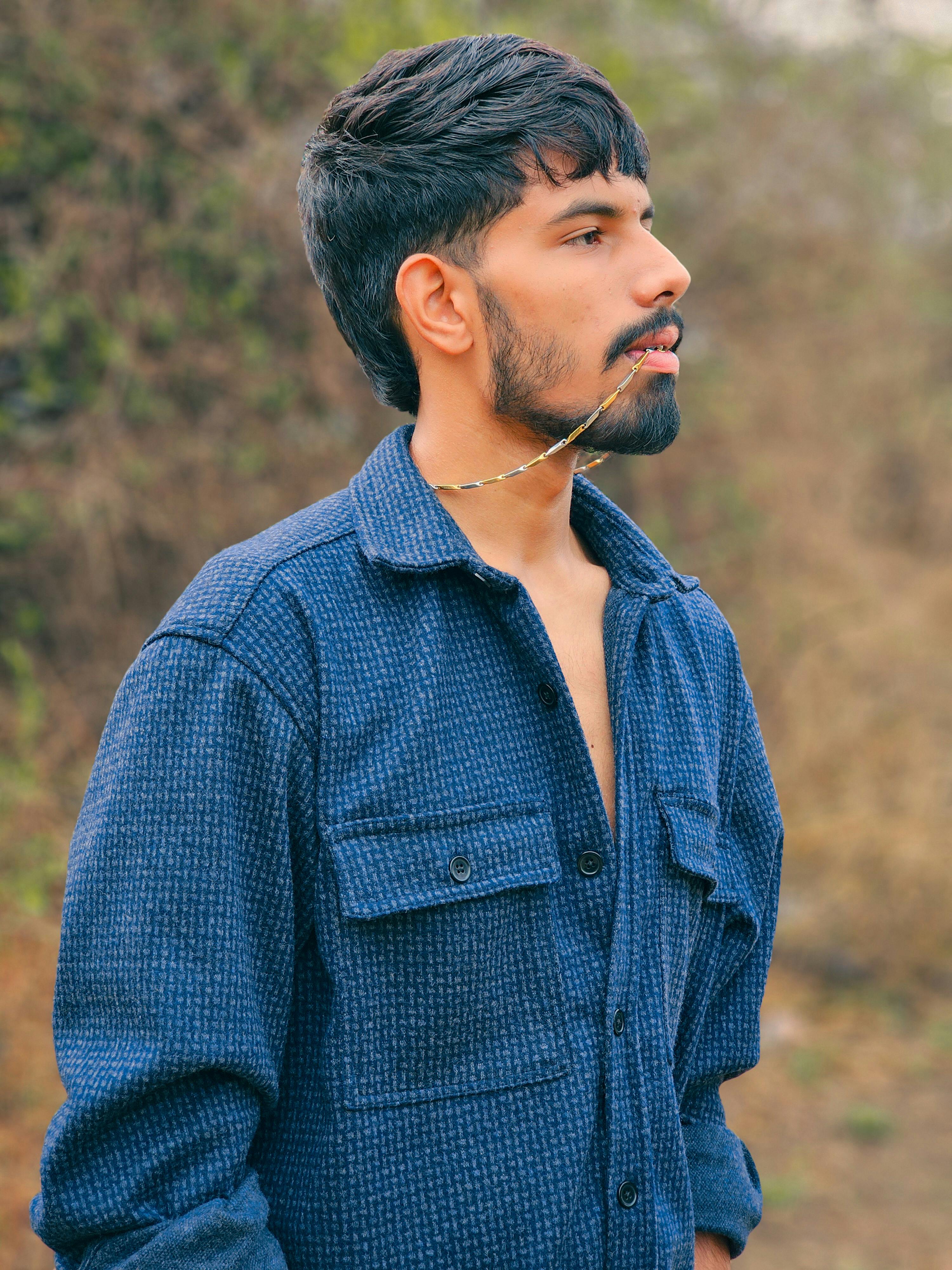 Side profile portrait of a man in a blue shirt outdoors with a thoughtful expression.