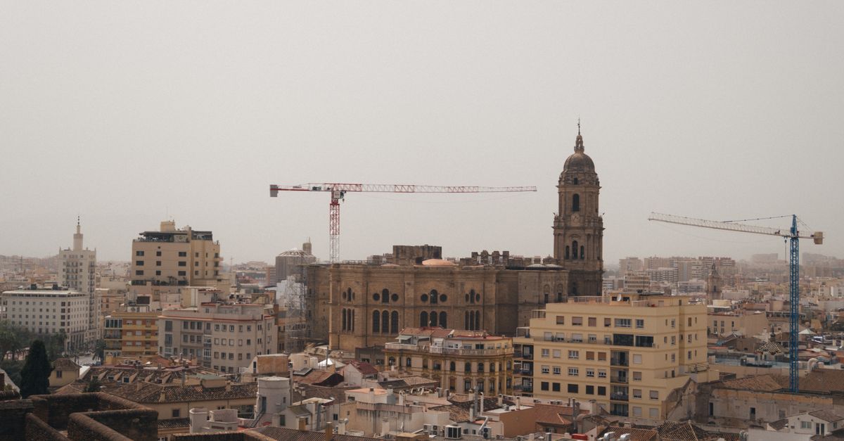 A stunning urban landscape featuring Malaga Cathedral amidst cranes and city buildings.