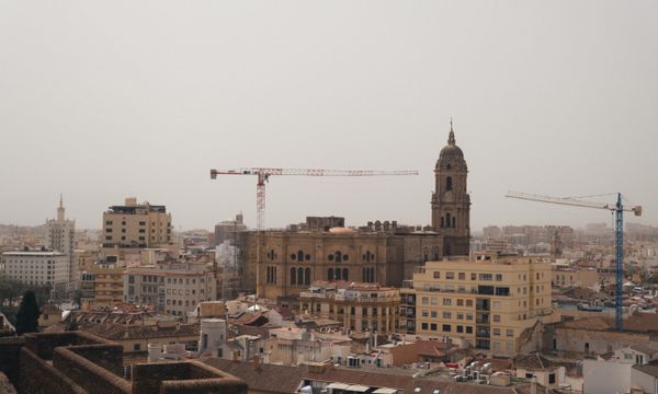 A stunning urban landscape featuring Malaga Cathedral amidst cranes and city buildings.