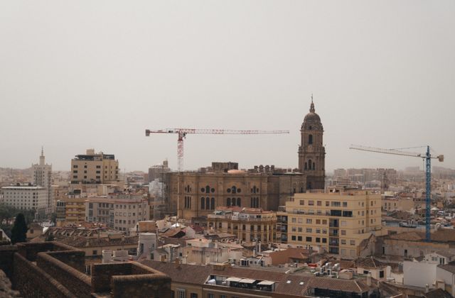 A stunning urban landscape featuring Malaga Cathedral amidst cranes and city buildings. — arriving in Málaga