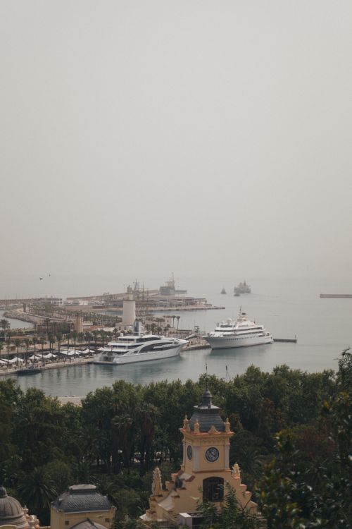 Free A serene view of Malaga harbor, featuring luxurious yachts docked amidst historic architecture. Stock Photo