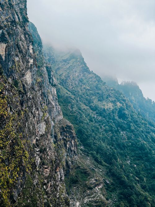 Free Breathtaking view of a steep mountain cliff shrouded in mist, showcasing rugged terrain and lush greenery. Stock Photo