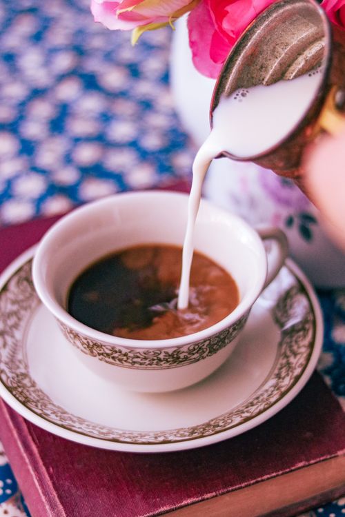 Free Close-up of milk being poured into a vintage coffee cup with floral decoration. Stock Photo