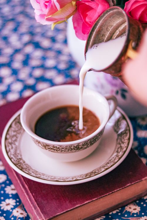 Free Close-up of milk being poured into a cup of coffee with a floral backdrop, creating a cozy atmosphere. Stock Photo