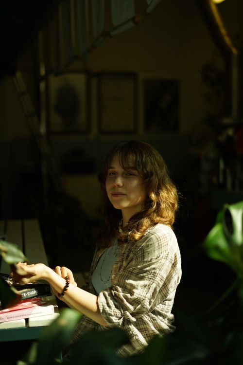 Free A young woman sits indoors, bathed in sunlight, creating a warm and relaxed atmosphere. Stock Photo