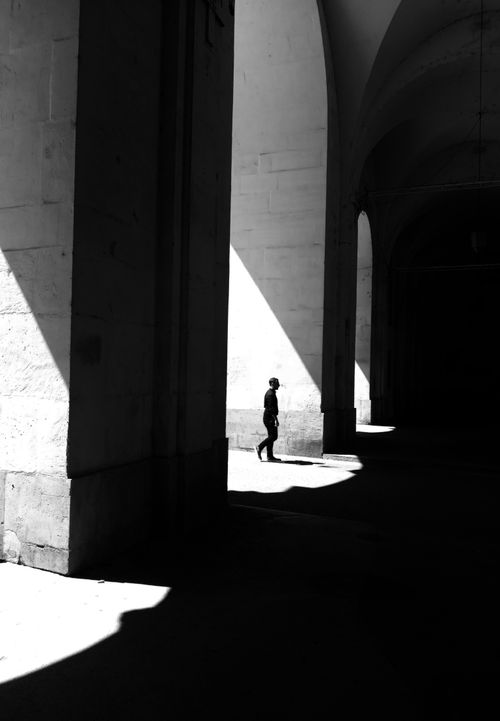 Free Dramatic black and white photo of a silhouette in a sunlit arched passage in Nancy, France. Stock Photo