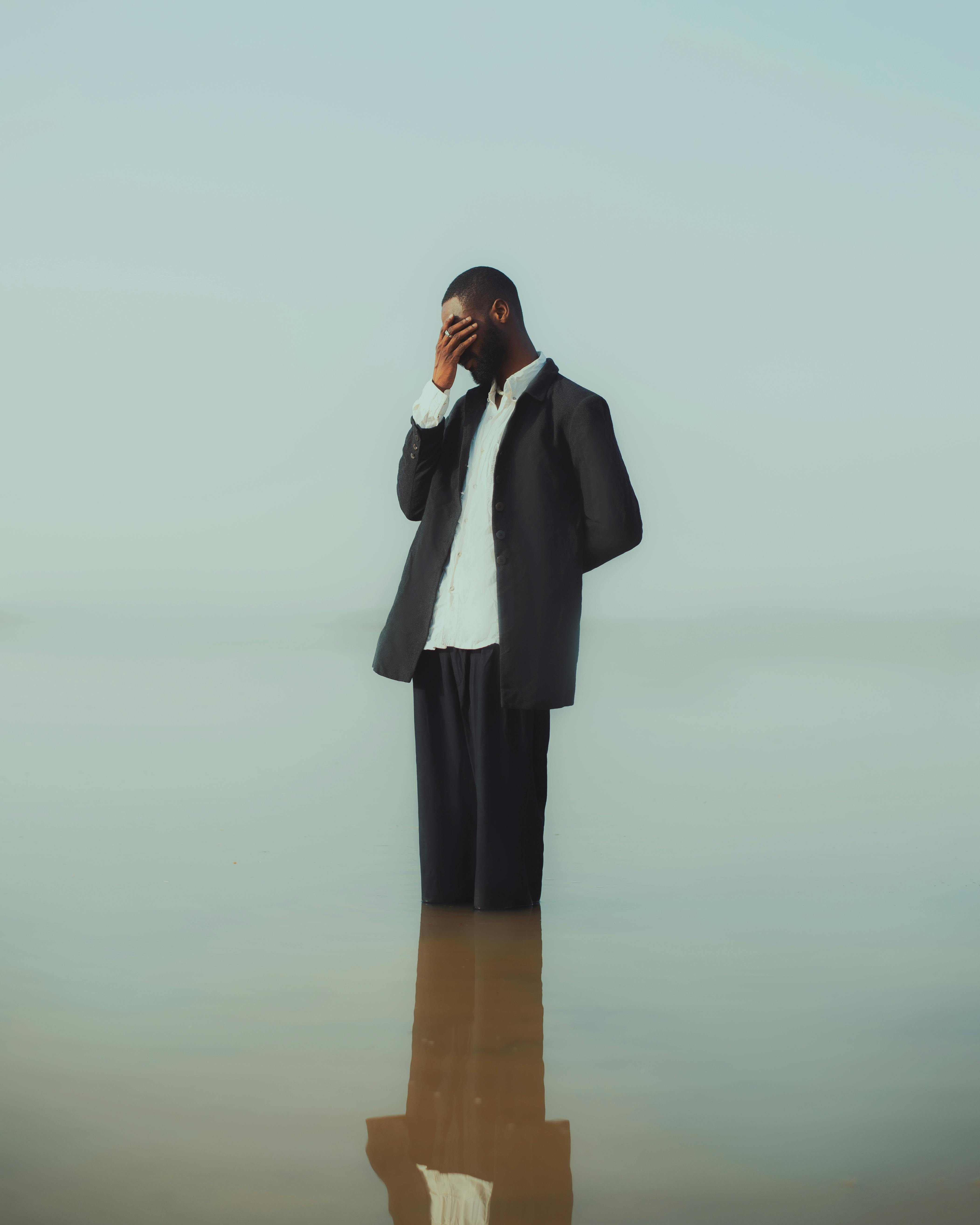 A pensive man in a suit stands in water reflecting deep thought or introspection.