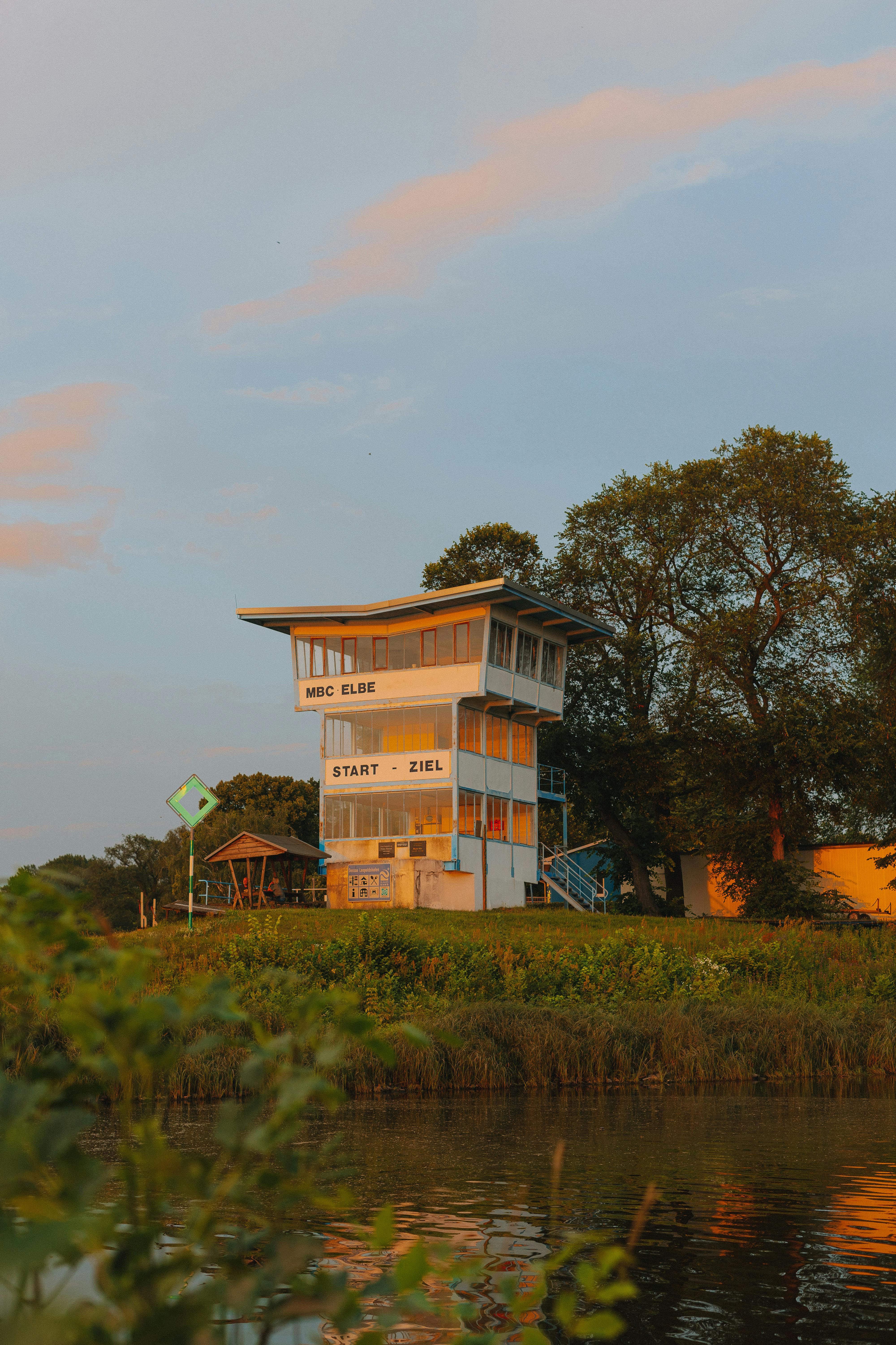 A charming riverside building amidst trees during sunset, with calm surroundings.
