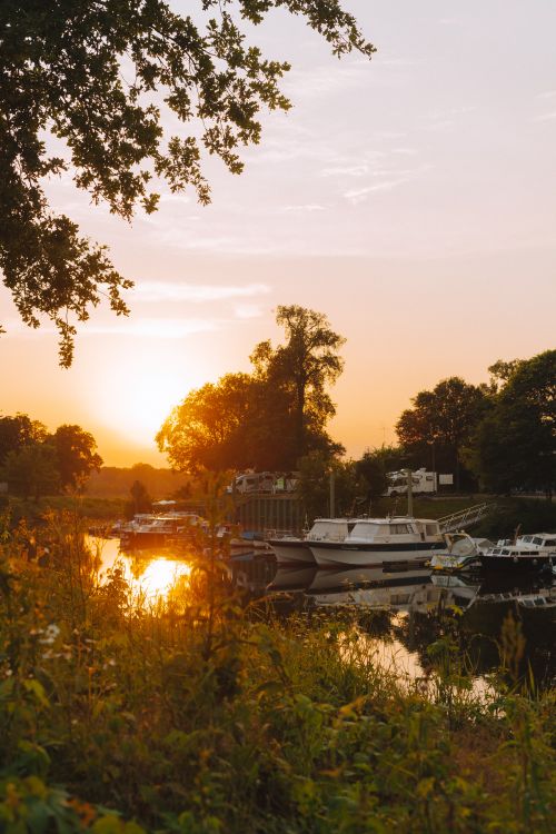 Free Tranquil scene of boats on a canal surrounded by trees at sunset, reflecting golden hues on the water. Stock Photo