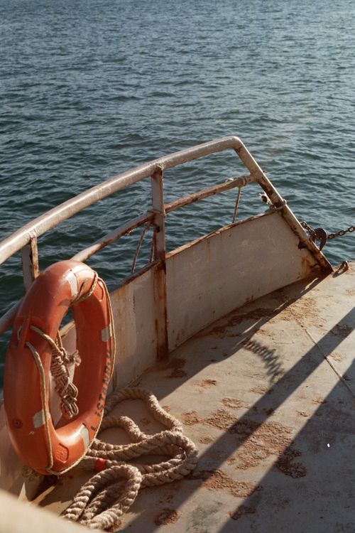 Free A rustic ship deck featuring a life buoy with a view of the sea. Ideal for maritime safety themes. Stock Photo