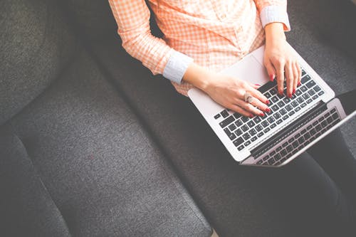 Person, Die Auf Grauem Sofa Sitzt, Während Sie Macbook Benutzt