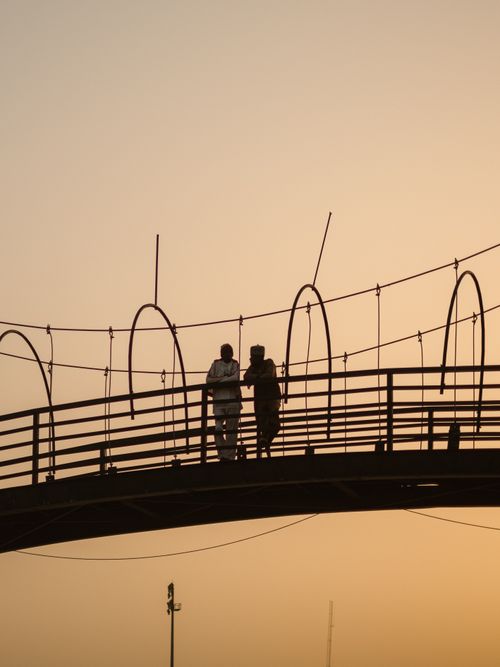 Free Silhouetted figures walking on a footbridge against a Kaduna sunset sky. Stock Photo