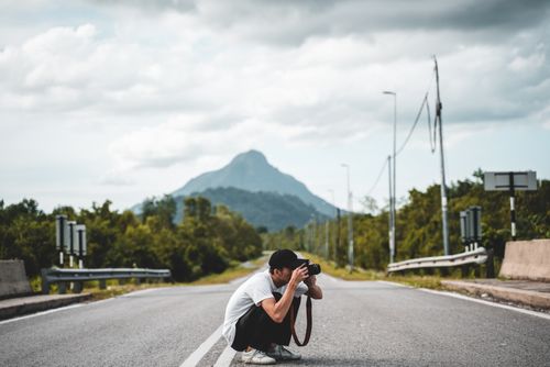 Free Man photographing on a quiet mountain road, capturing natural beauty. Stock Photo