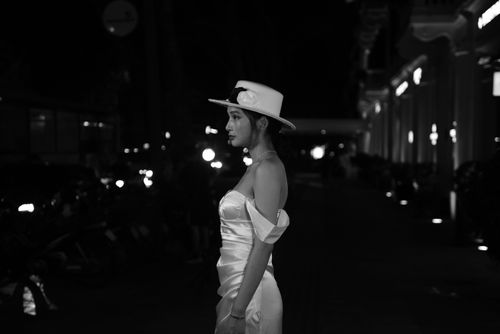 Free Elegant woman in a white dress and hat, posing on a dimly lit street at night. Stock Photo