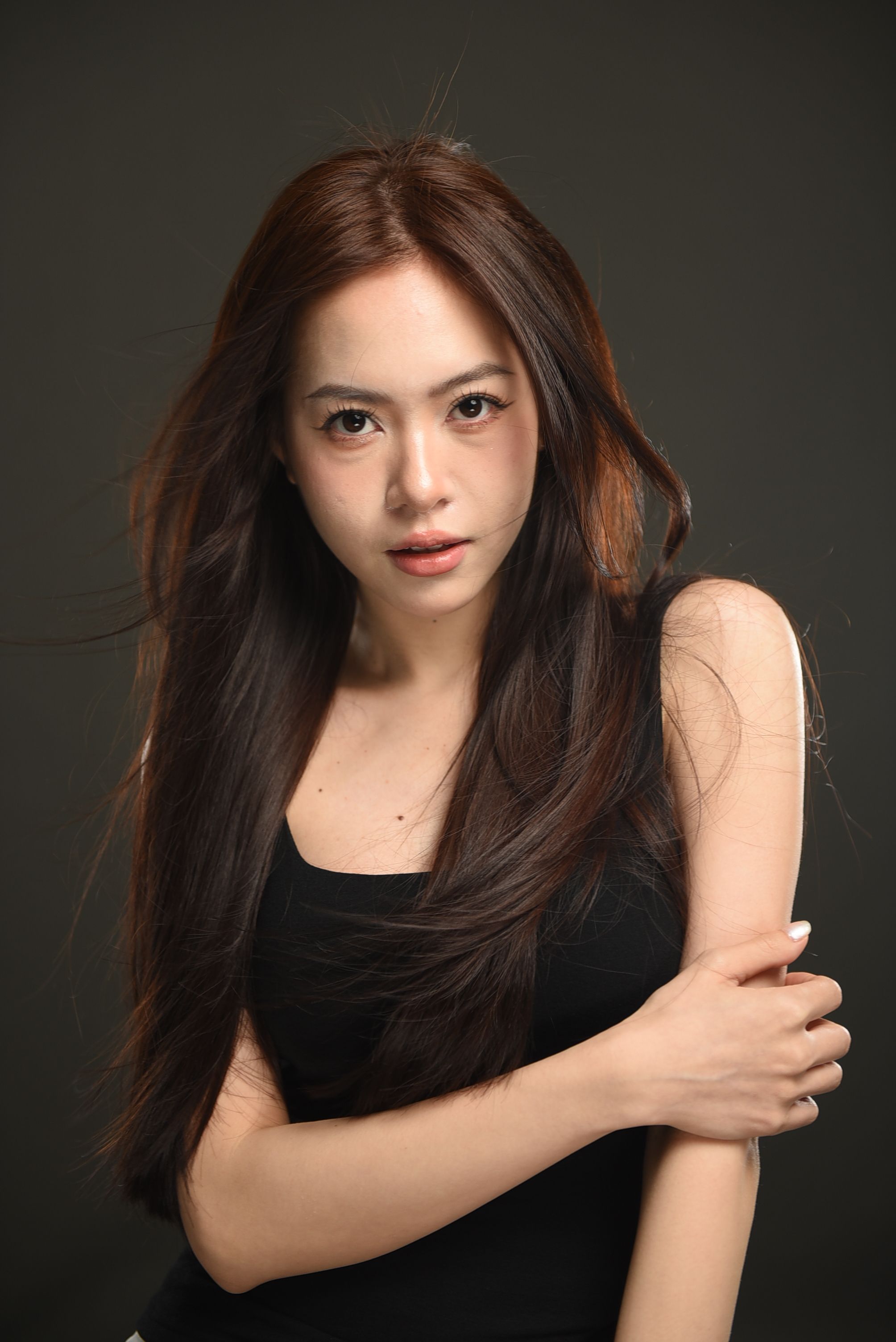 Close-up portrait of an Asian woman with long hair in a black tank top in studio lighting.