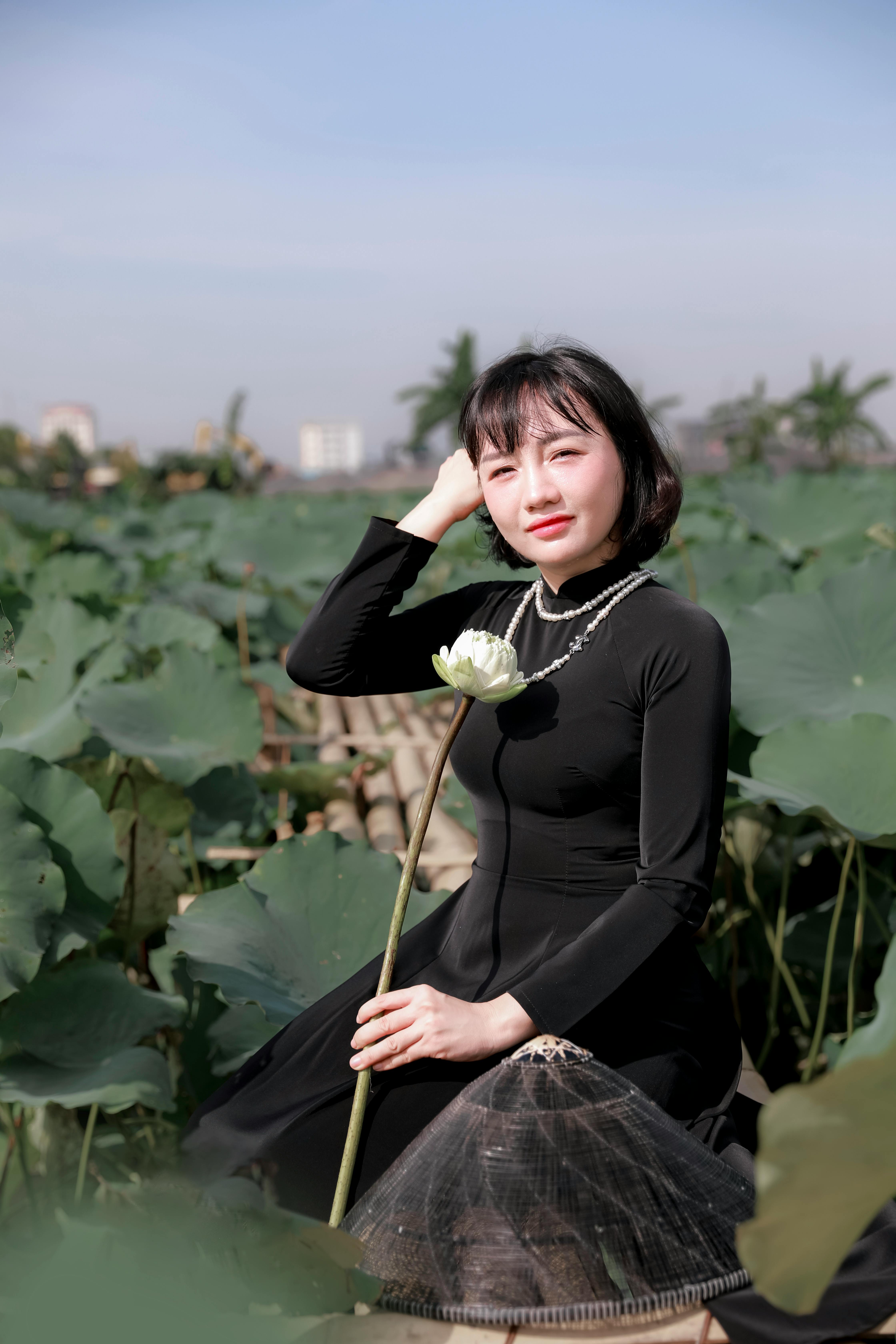 Vietnamese woman in ao dai sitting in a lotus field, smiling under the sun.