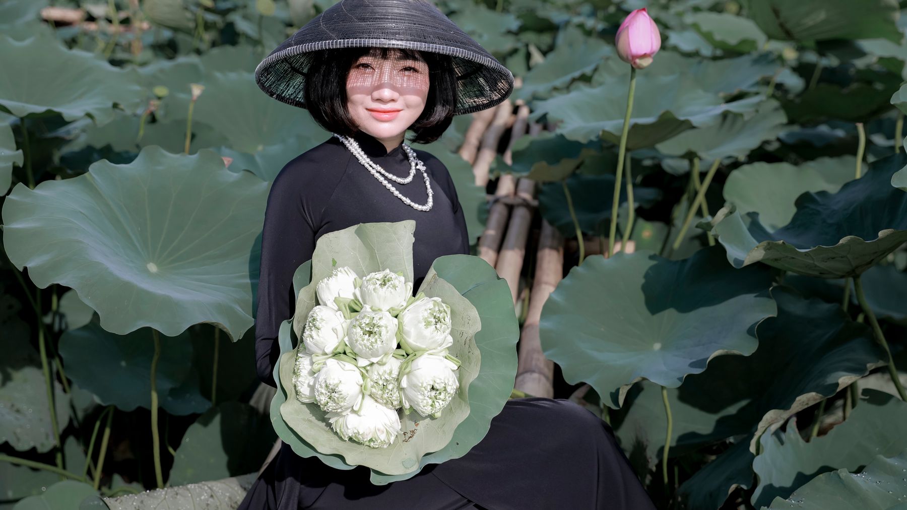 A graceful Vietnamese woman in an ao dai with conical hat amidst lush lotus flowers.