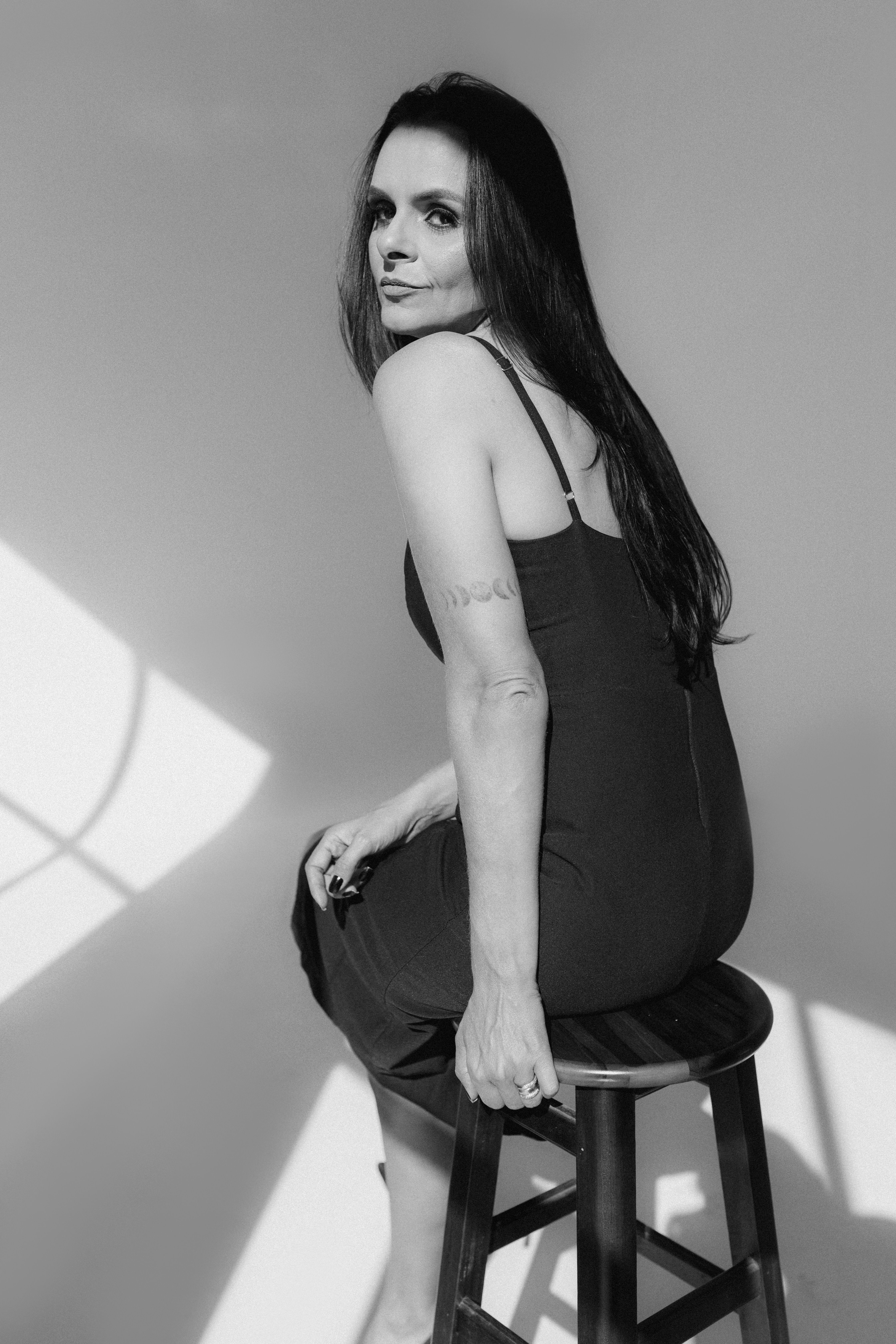 Black and white portrait of a woman in a dress, seated on a stool in a Brazilian studio.