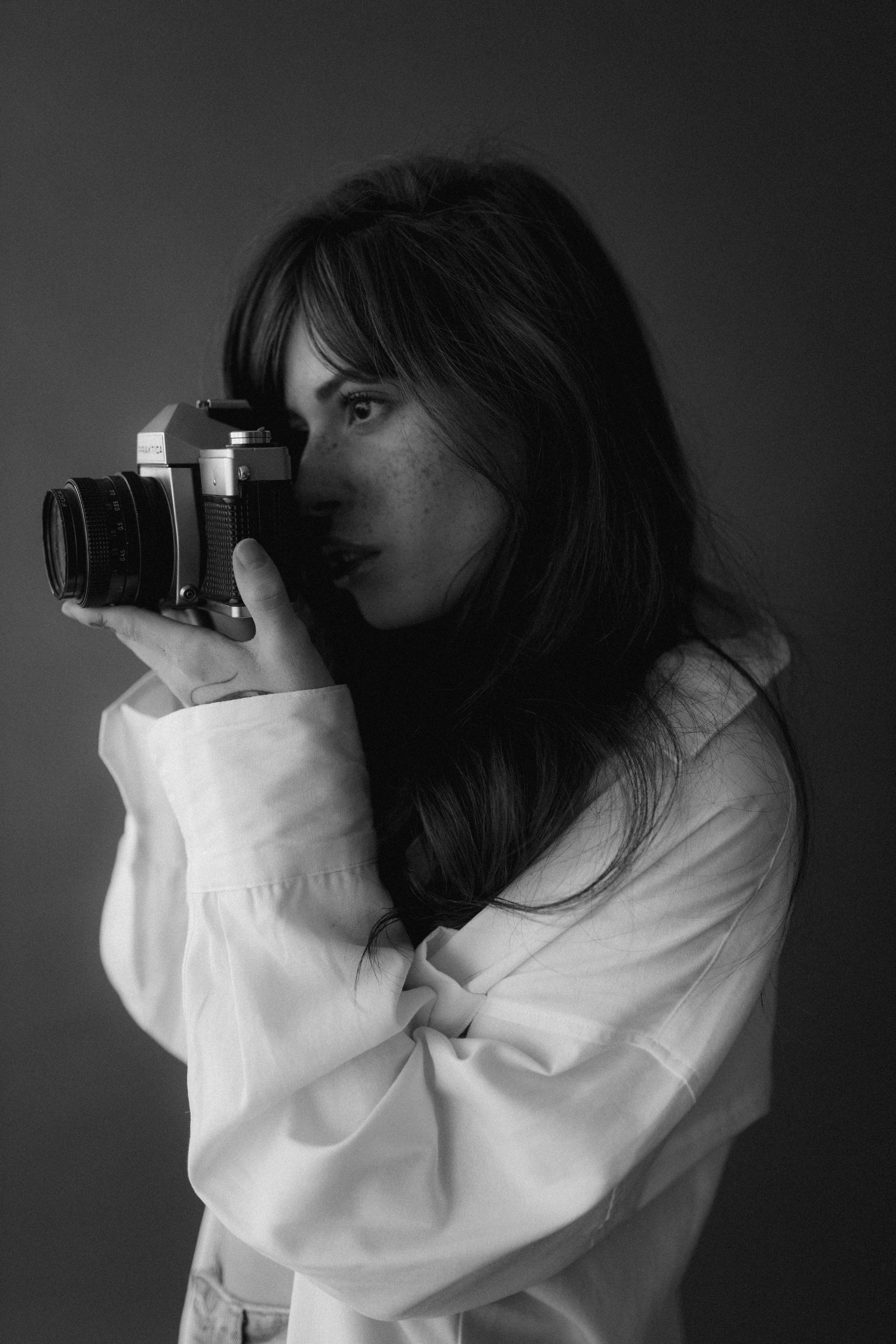 Artistic black and white portrait of a woman in a studio holding a vintage camera.