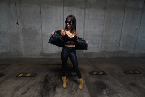 Free Trendy woman in leather outfit and sunglasses posing confidently in an underground parking lot. Stock Photo