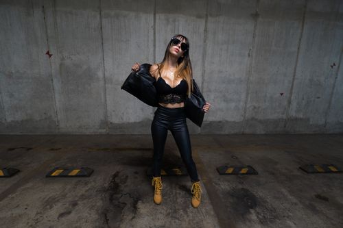 Free Stylish woman in black leather and lingerie poses confidently in an urban parking space. Stock Photo