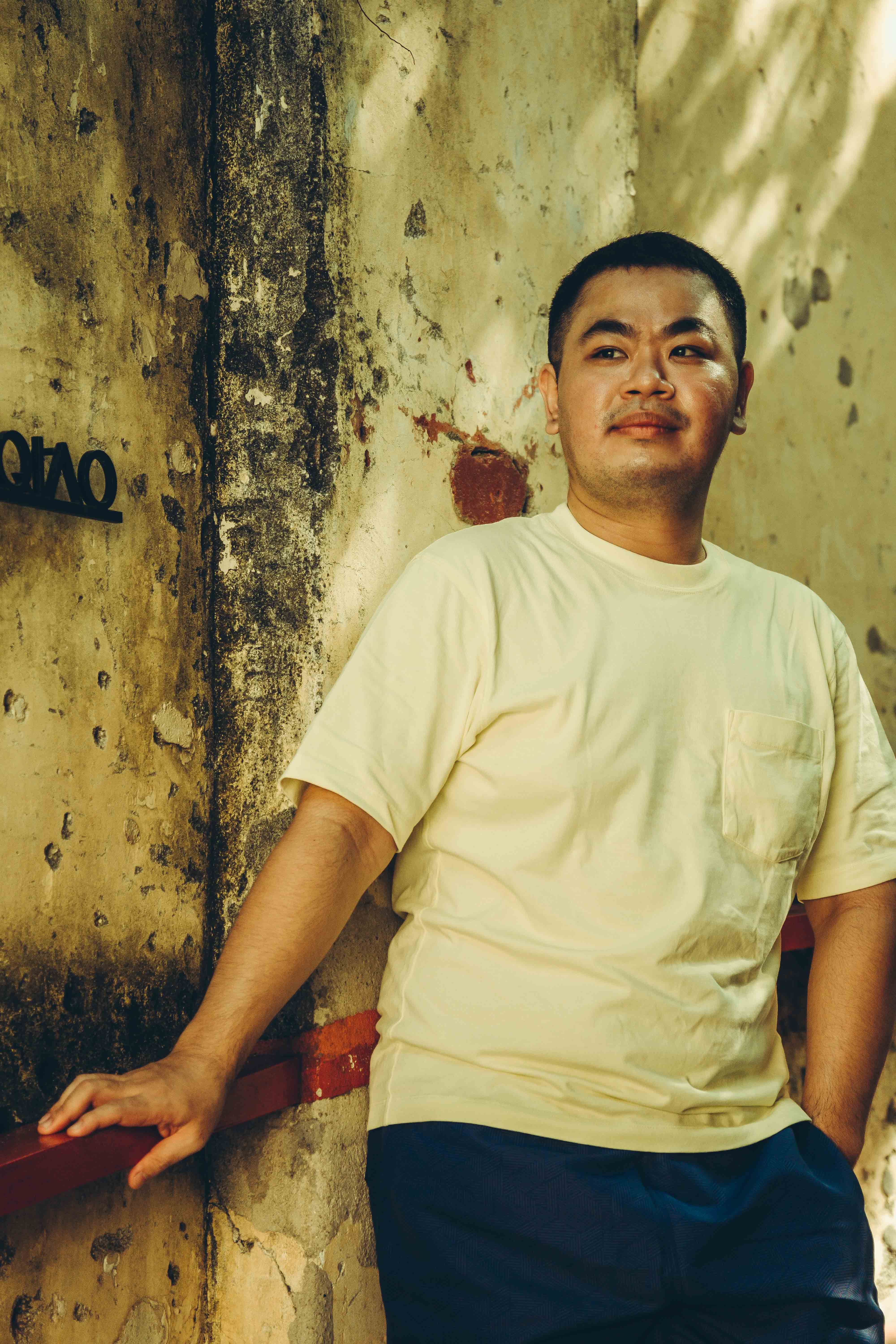Portrait of a man leaning against a textured wall in Kuala Lumpur.
