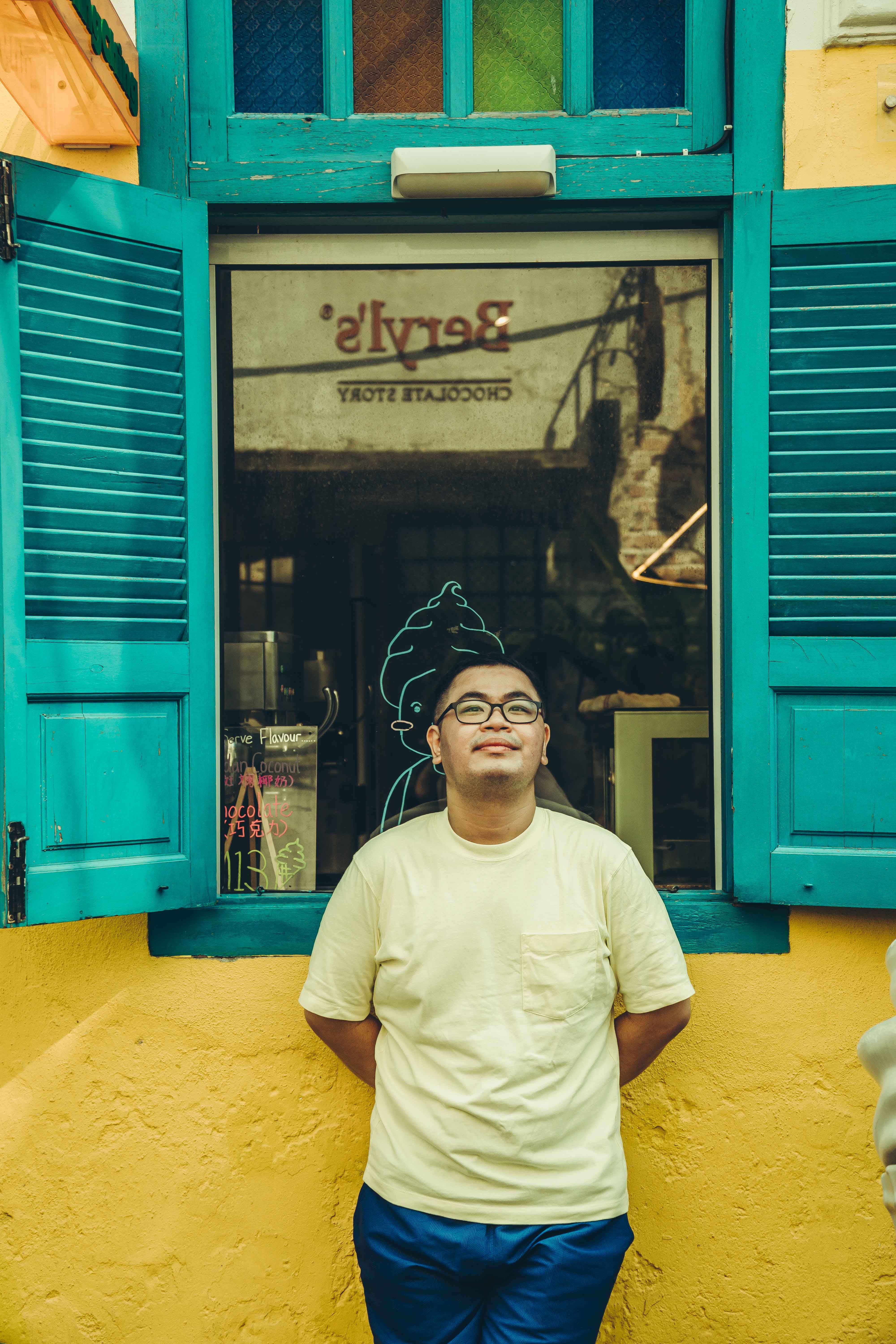A man leans casually against a colorful window in Kuala Lumpur, Malaysia, enjoying a sunny day.
