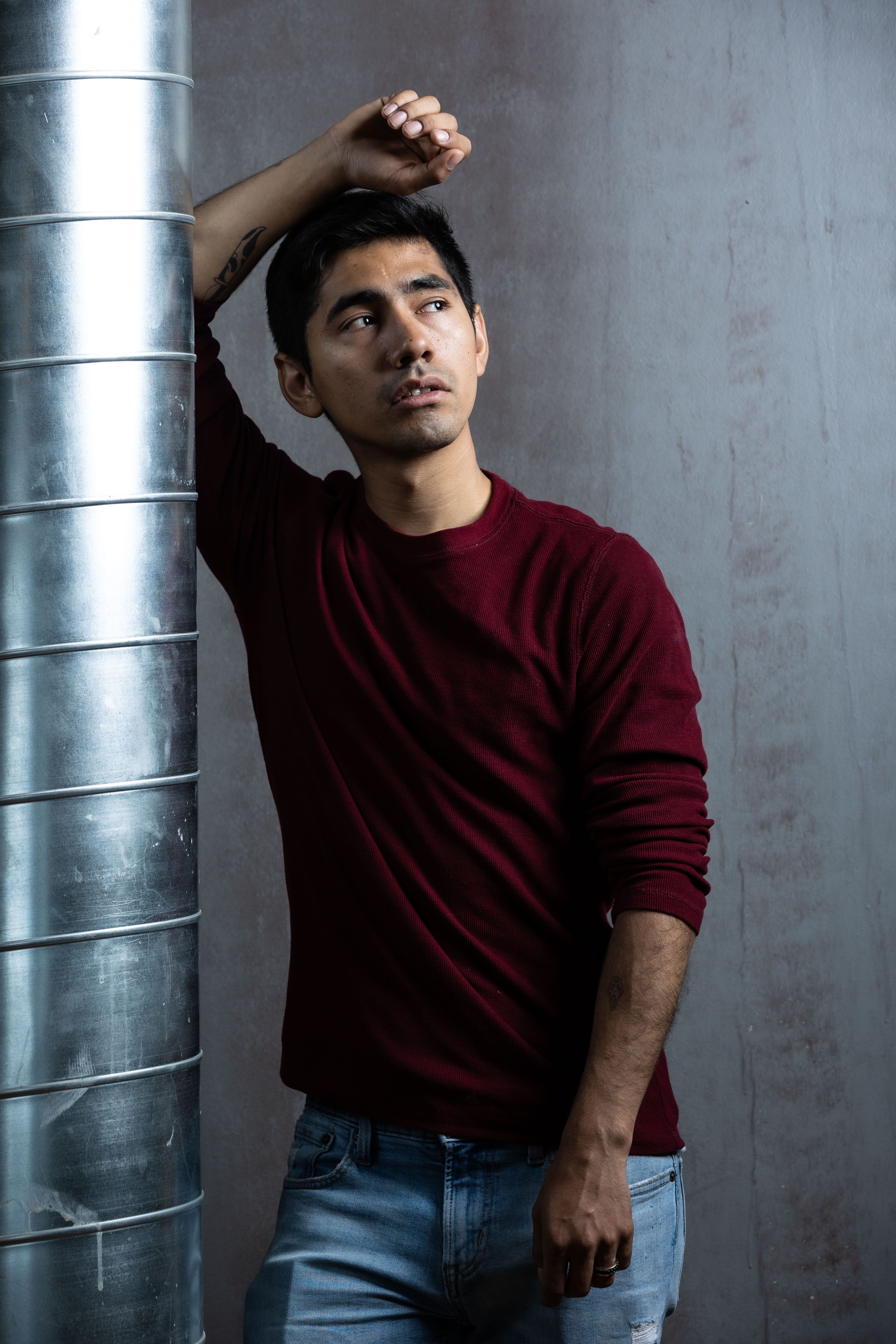Urban portrait photograph of a young man in casual attire leaning against a metal pillar in Chicago.