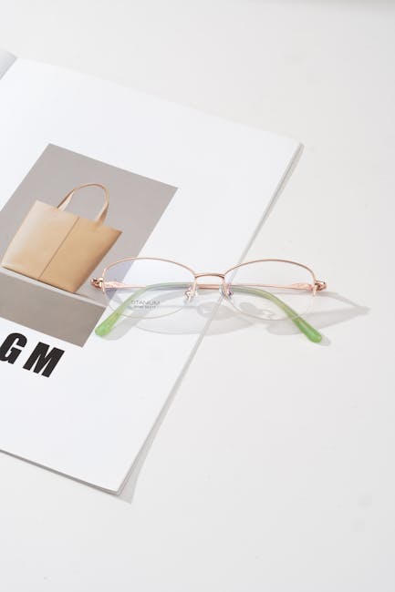 A pair of sleek eyeglasses with green accents rest on an open fashion magazine, emphasizing modern style and simplicity.