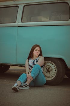 Young woman in casual attire sitting by a vintage van, exuding retro vibes.