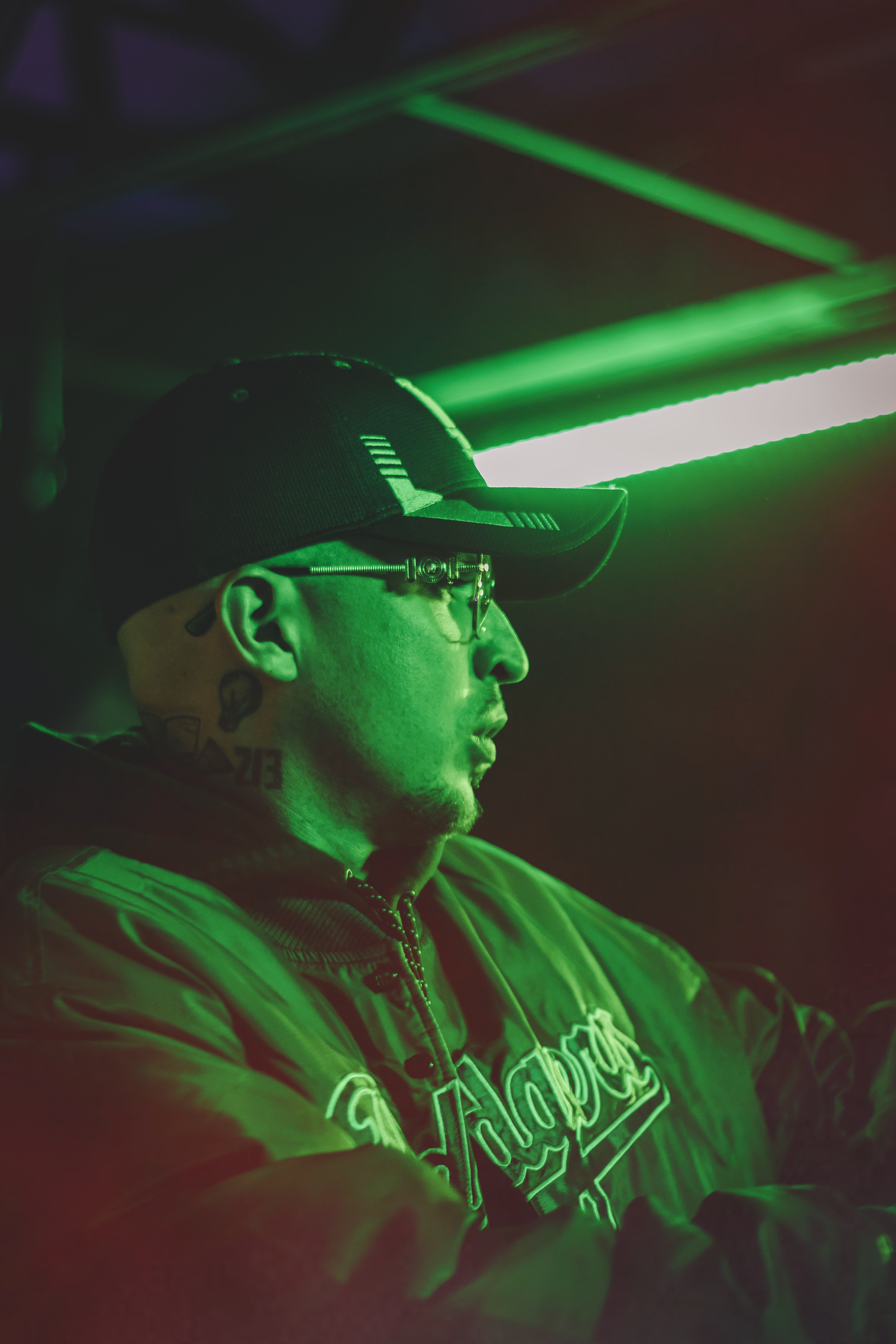 A man wearing a cap and eyeglasses in green light at a night party scene.