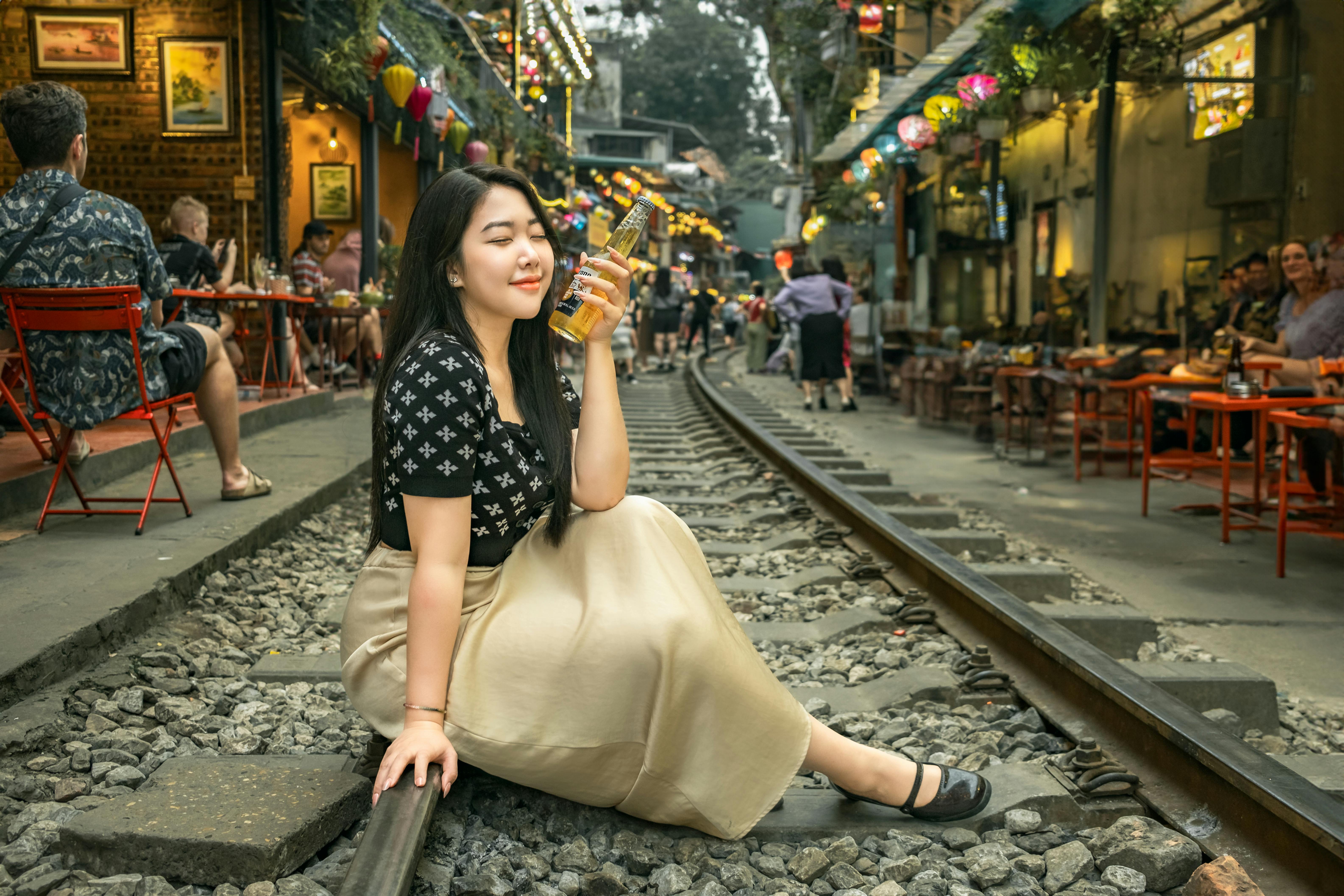 A woman enjoying a drink while sitting on train tracks in Hanoi's vibrant train street.