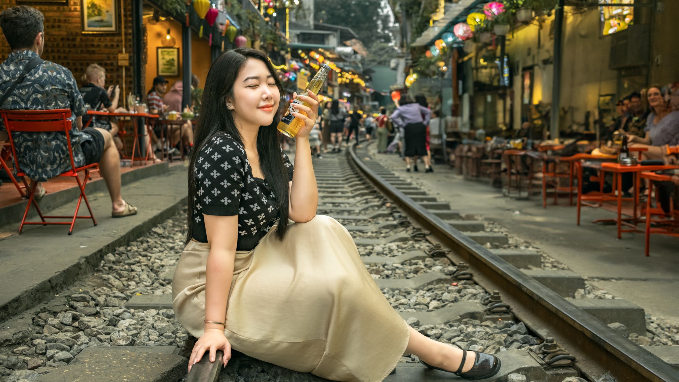 A woman enjoying a drink while sitting on train tracks in Hanoi's vibrant train street.