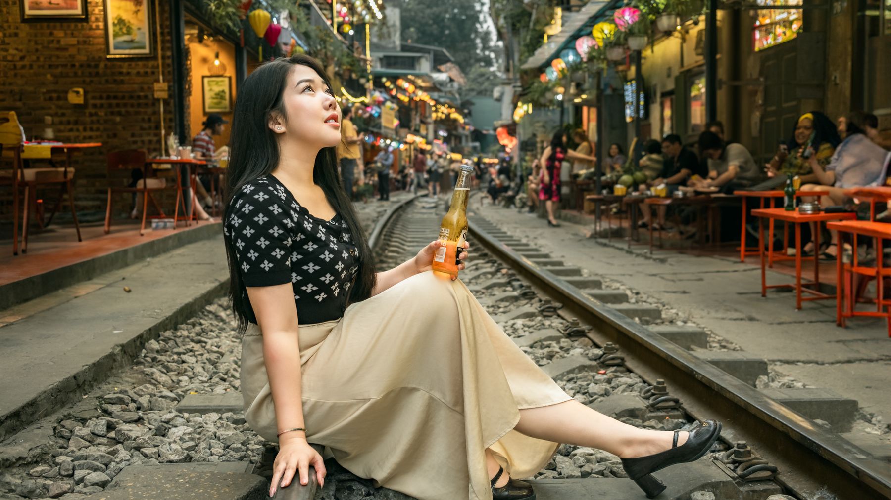 Woman enjoying a drink while sitting on railway tracks in a bustling street.