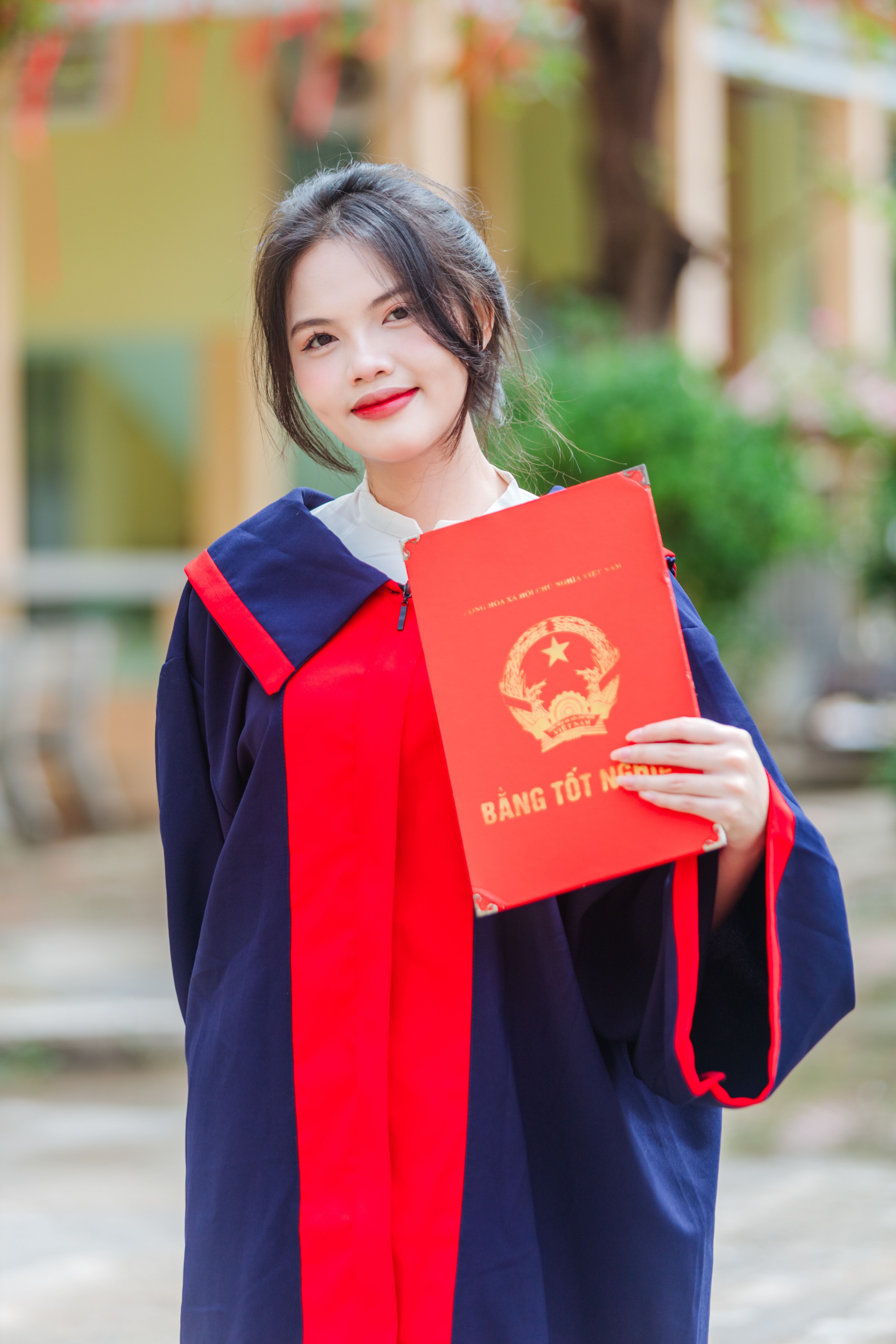 Woman in graduation gown holding diploma outdoors during daytime.
