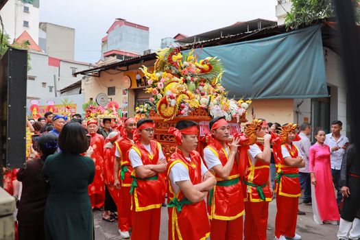 Asian parade featuring participants in red traditional attire carrying a decorated statue through city streets.