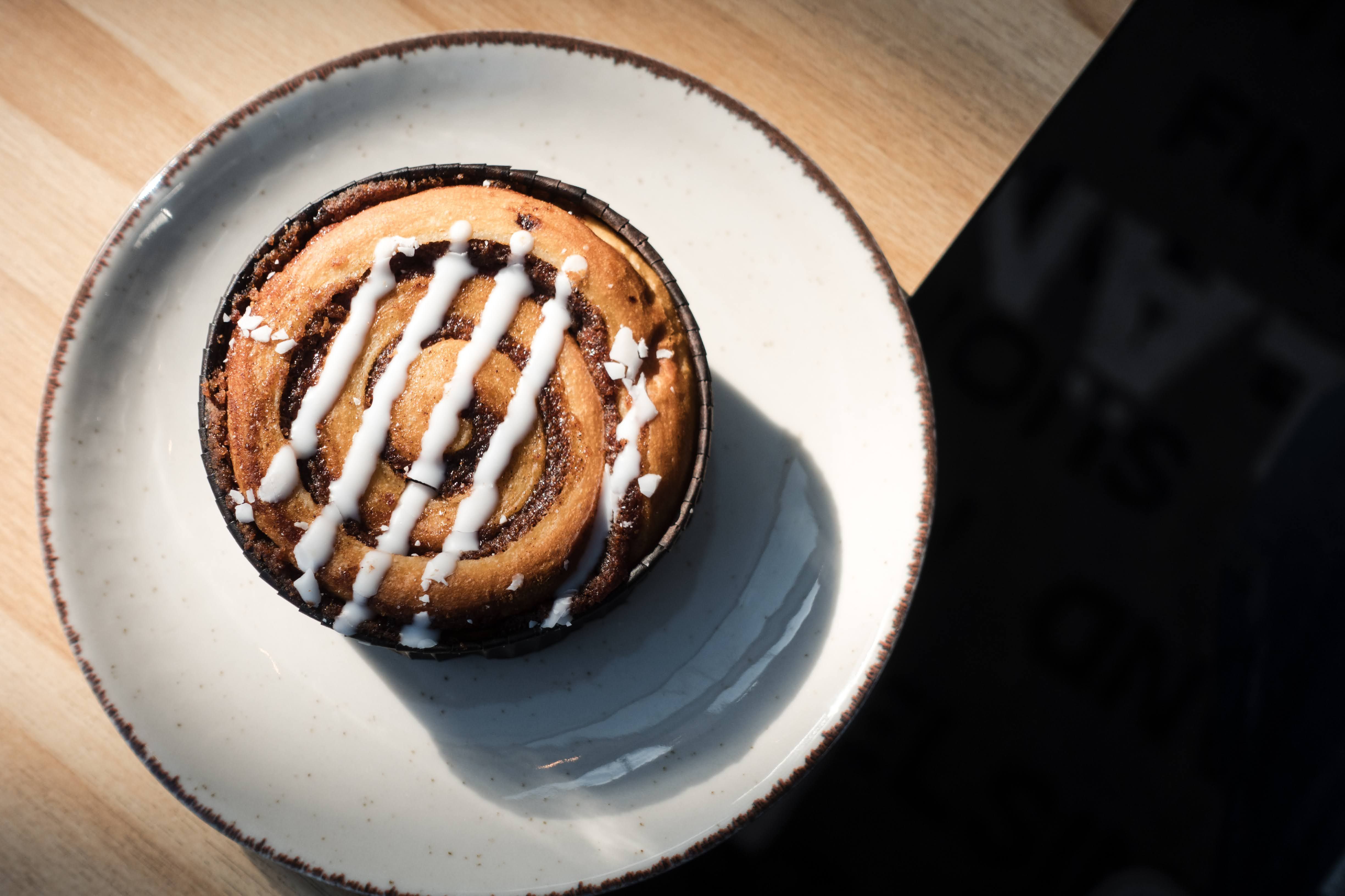 A top view of a cinnamon roll with icing on a plate, bathed in warm sunlight.