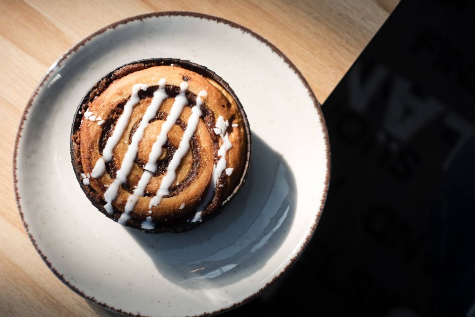 A top view of a cinnamon roll with icing on a plate, bathed in warm sunlight.