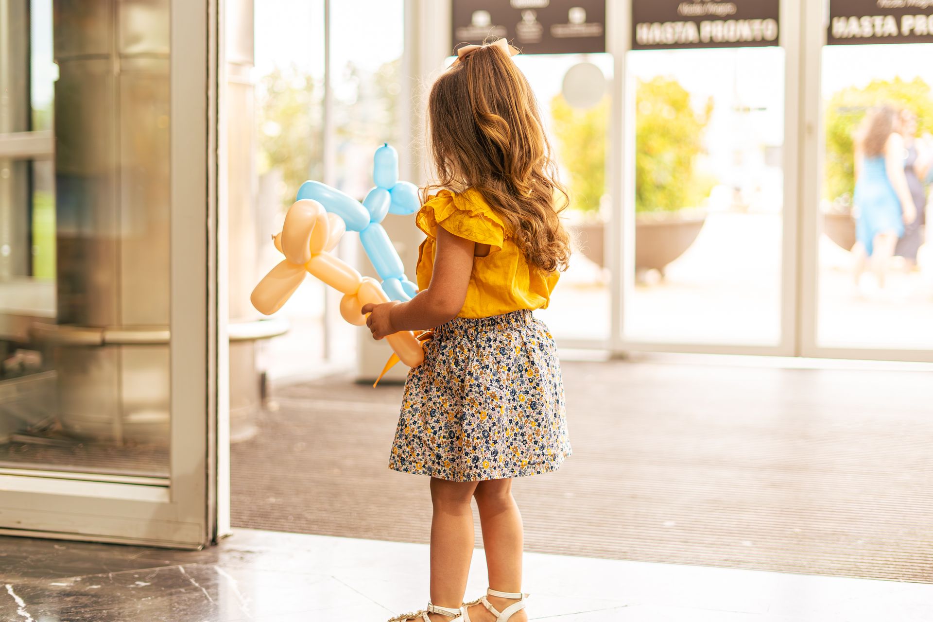 Back View of Girl Standing in Automatic Door Holding Balloon Animals