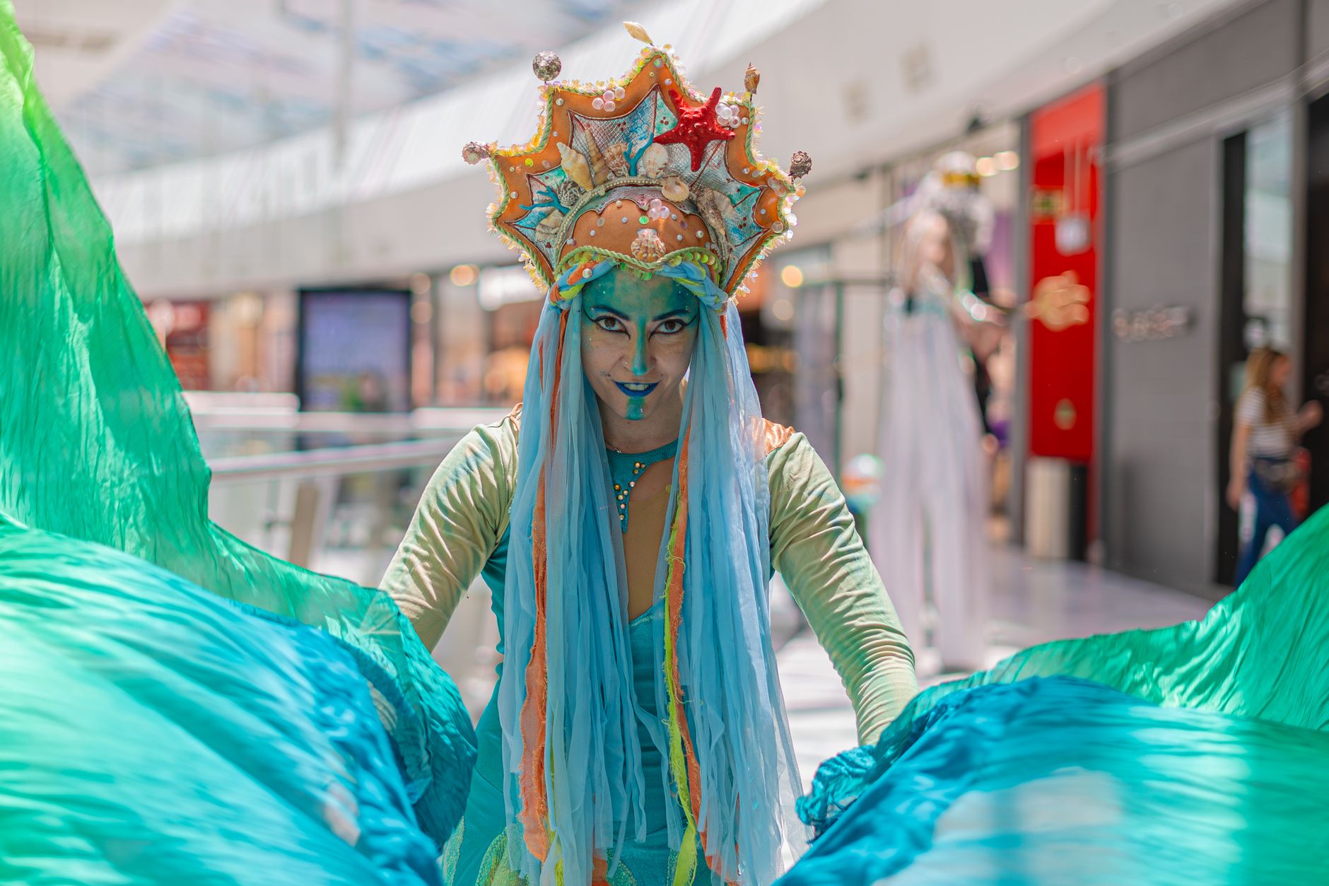 Colorful mermaid-costumed performer entertaining at a mall with vibrant makeup and elaborate costume.