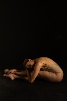 A flexible ballerina striking an artistic pose in a dimly lit studio setting.