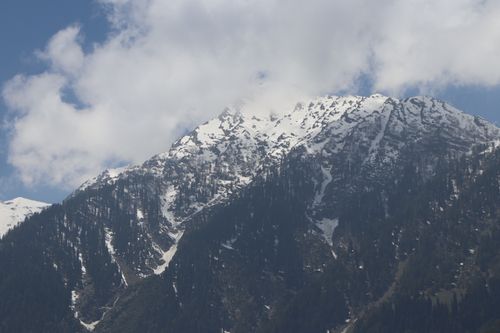 Free A scenic view of snow-covered mountain peaks beneath a cloudy blue sky. Stock Photo