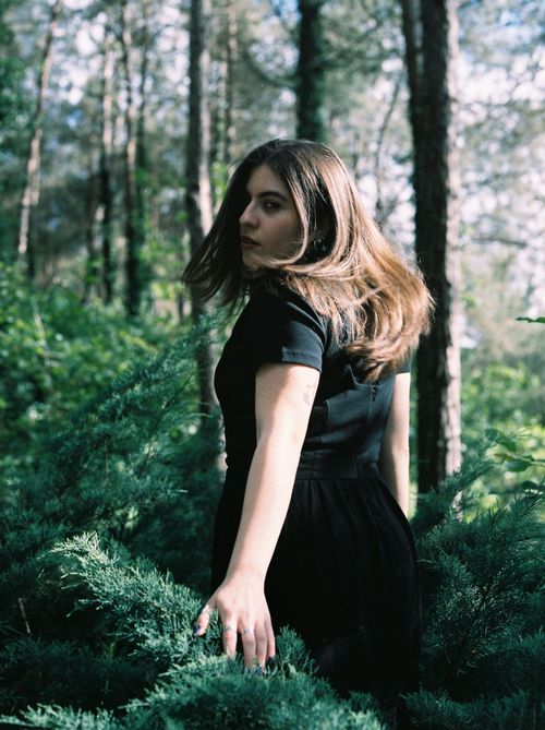 Free A woman in a black dress stands amidst lush greenery, embodying nature's elegance. Stock Photo