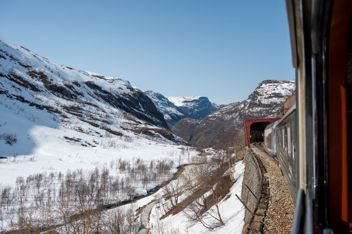 The Flam Railway train passing through snow-covered Norwegian landscapes alongside a deep fjord
